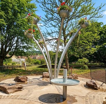 Image of a children's play area including play equipment with three long metal arms on which plants are growing